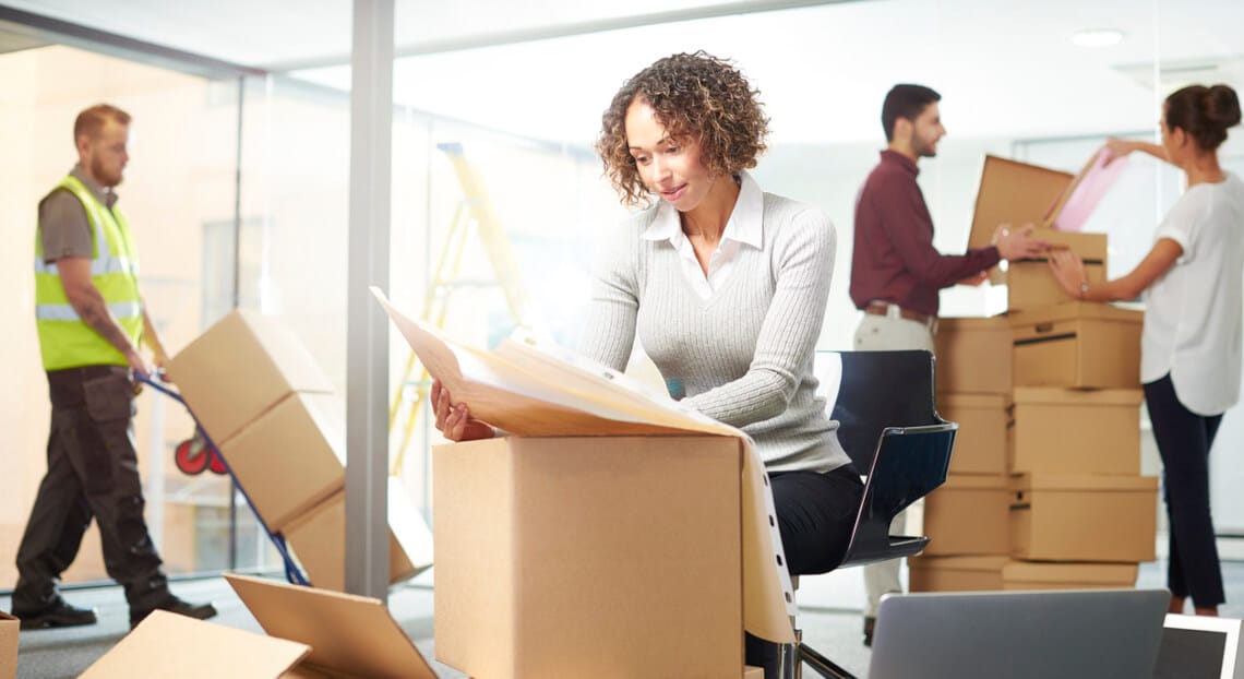 Young female entrepreneur coordinates office relocation plans in NYC, surrounded by moving boxes.