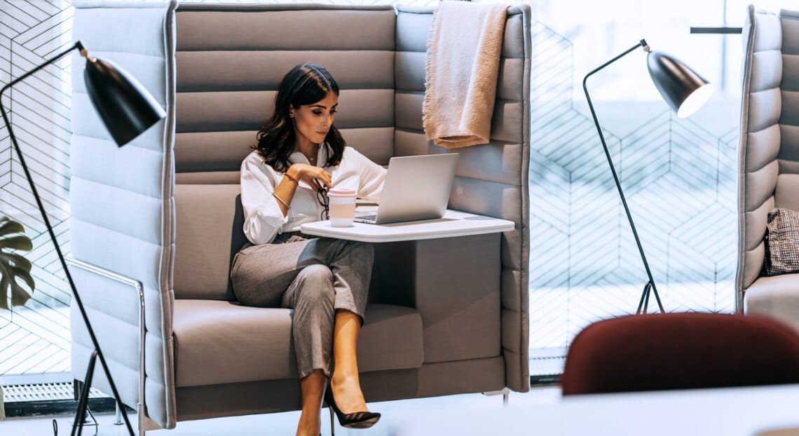 Mid adult businesswoman in NYC office, working on laptop at open space desk.