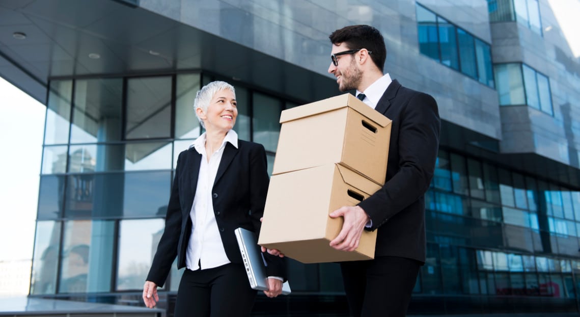 Business professionals with card boxes moving in front of NYC office buildings during relocation.