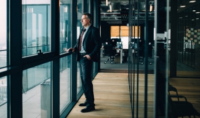 Businessman gazes out NYC window, pondering post-moratorium challenges for landlords and tenants.