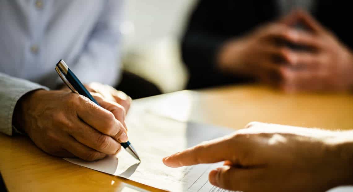 Unidentified individual in NYC signing a lease contract with a real estate agent.