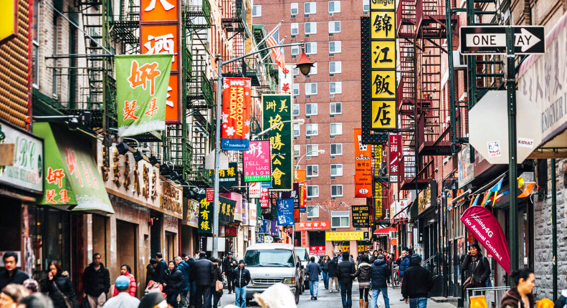 People in a vibrant NYC Chinatown street with colorful shops and restaurants.