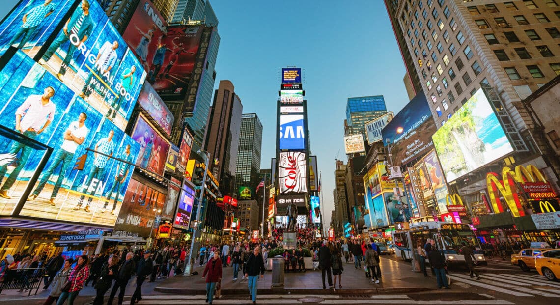 A crowded Times Square in New York City, with tourists and people sightseeing.