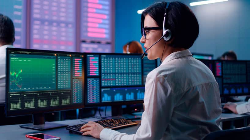 Young trader with headset reviews data on computer in a financial services office space, back view