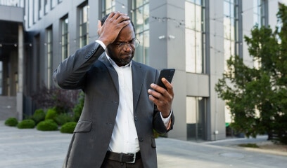 Disappointed businessman in NYC, facing office space challenges, smartphone in hand.