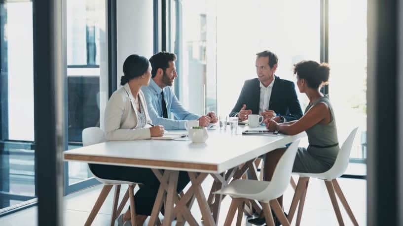 Four business people meeting in bright office with glass walls.