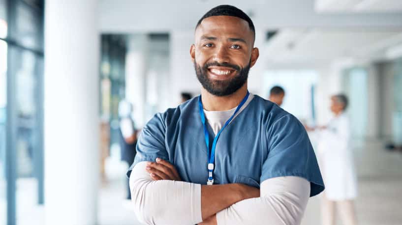 Confident male nurse in scrubs, standing in hospital hall, smiling with arms crossed