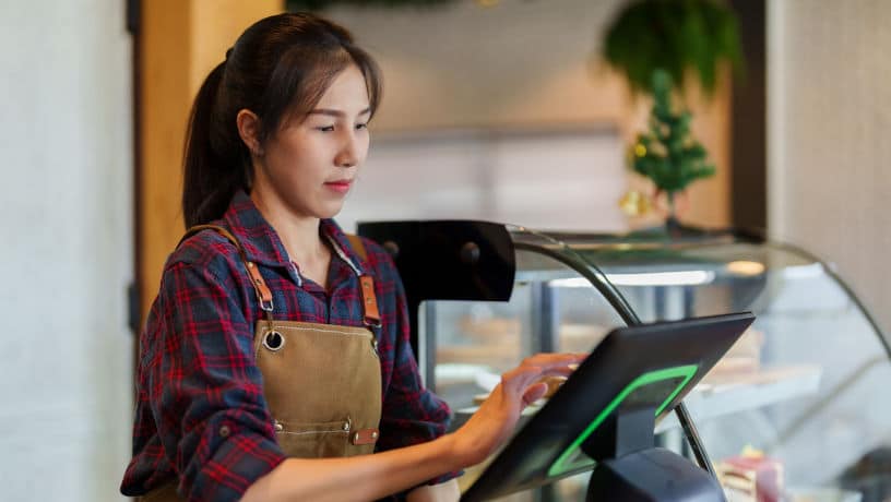 A bakery cafe owner is standing behind the counter, collecting money at the cash register. There is a machine at the front counter that can take orders. The photo is promoting retail space for rent in Manhattan, NYC.