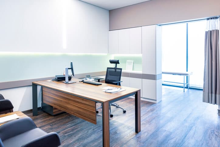 Empty private office with desk, white walls, and examination room.