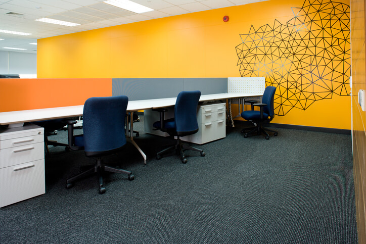 Office with yellow wall, partitioned cubicles and desks.