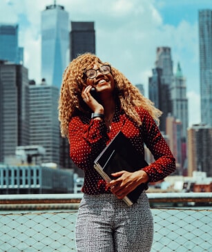 Smiling millennial entrepreneur on call, Downtown Manhattan skyline backdrop.