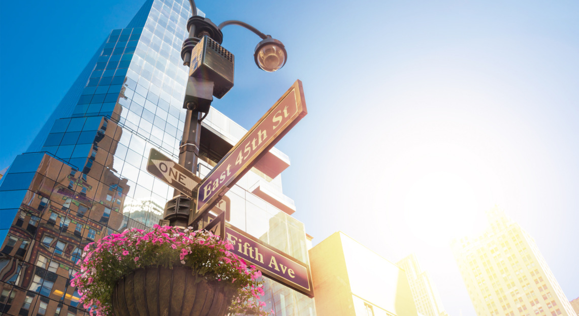Street sign at E 45th & Fifth Ave, NYC, with flowers and buildings.