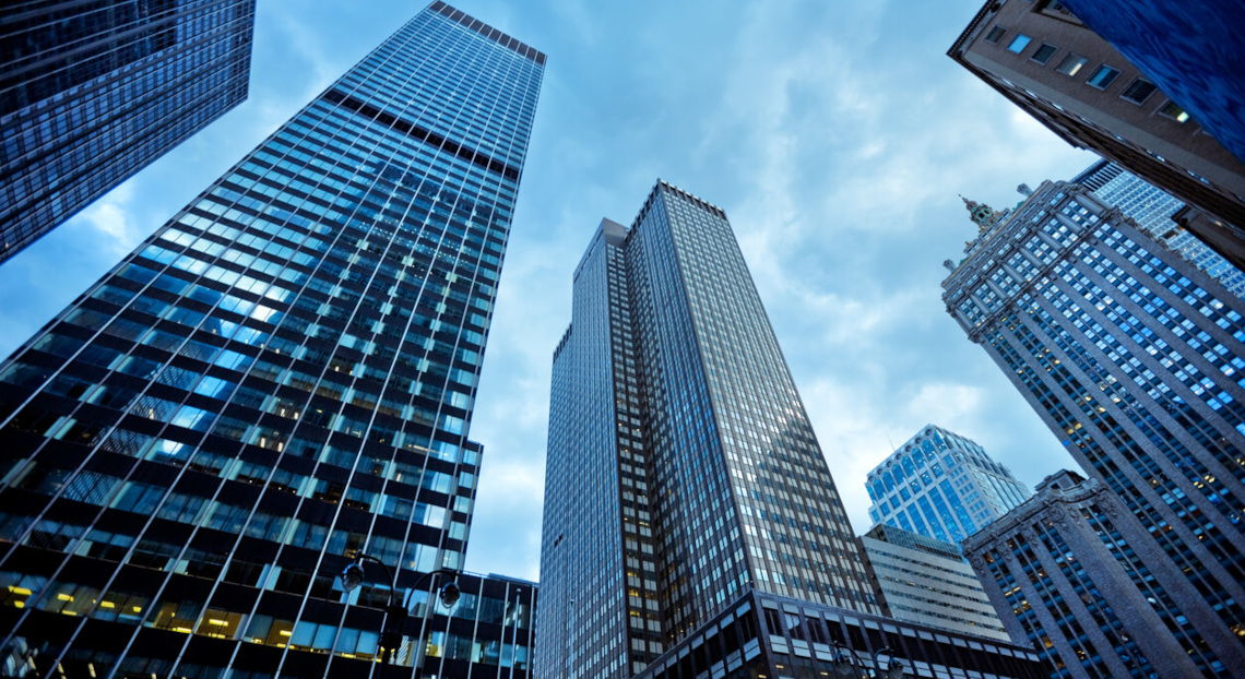 Glass-and-steel skyscrapers soar upward against a cloudy blue sky in Manhattan.
