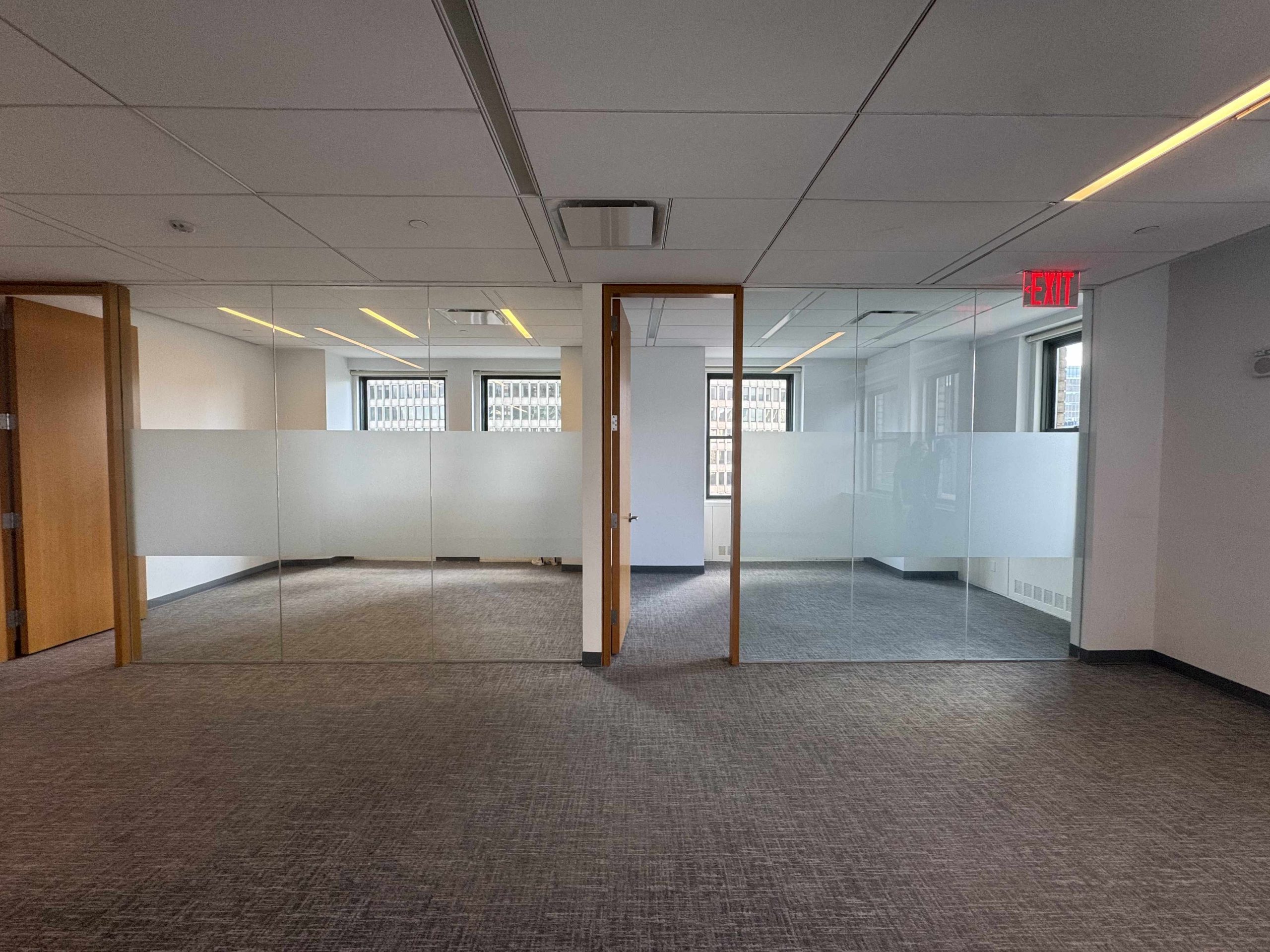 Modern office with glass walls, grey carpet, wood doors, and exit sign.
