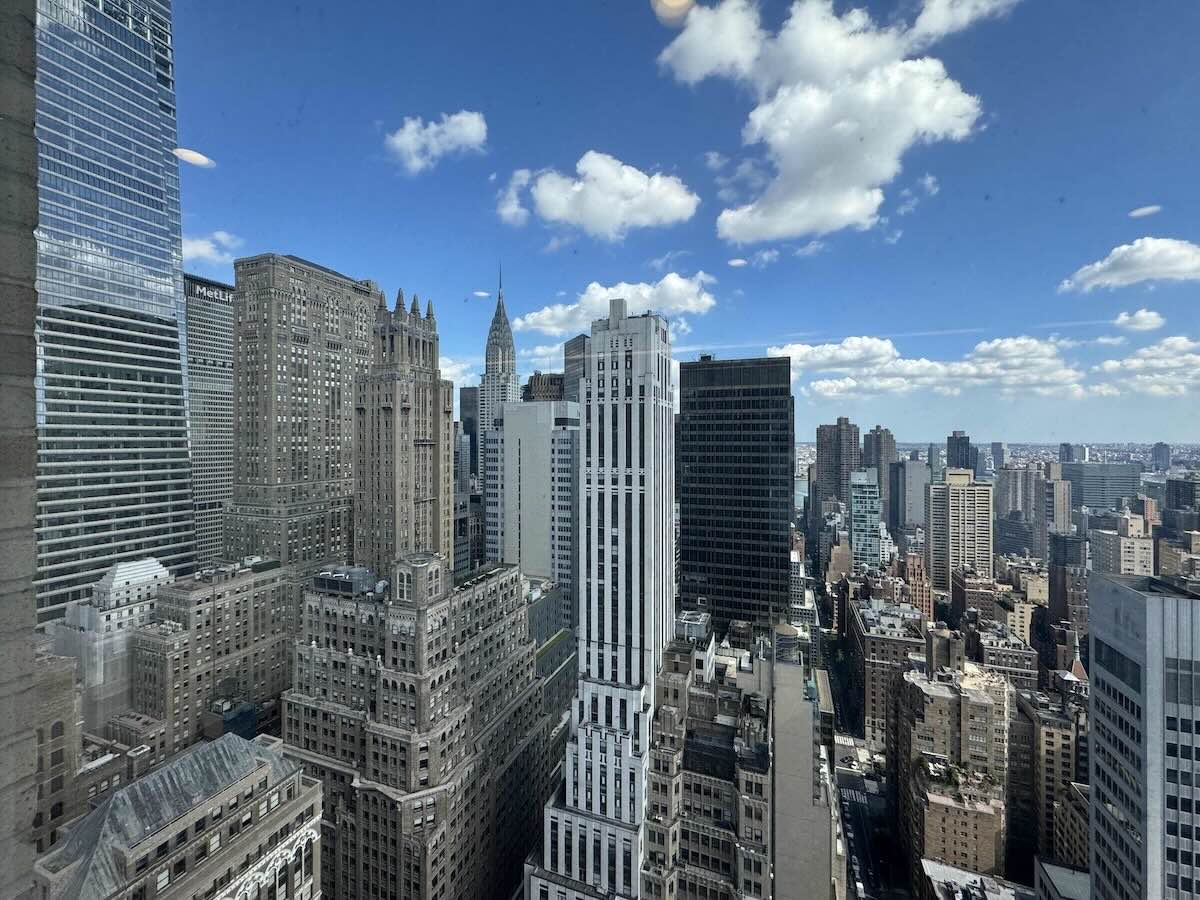 Cityscape of skyscrapers and historic buildings under a blue sky, seen from a high office floor.