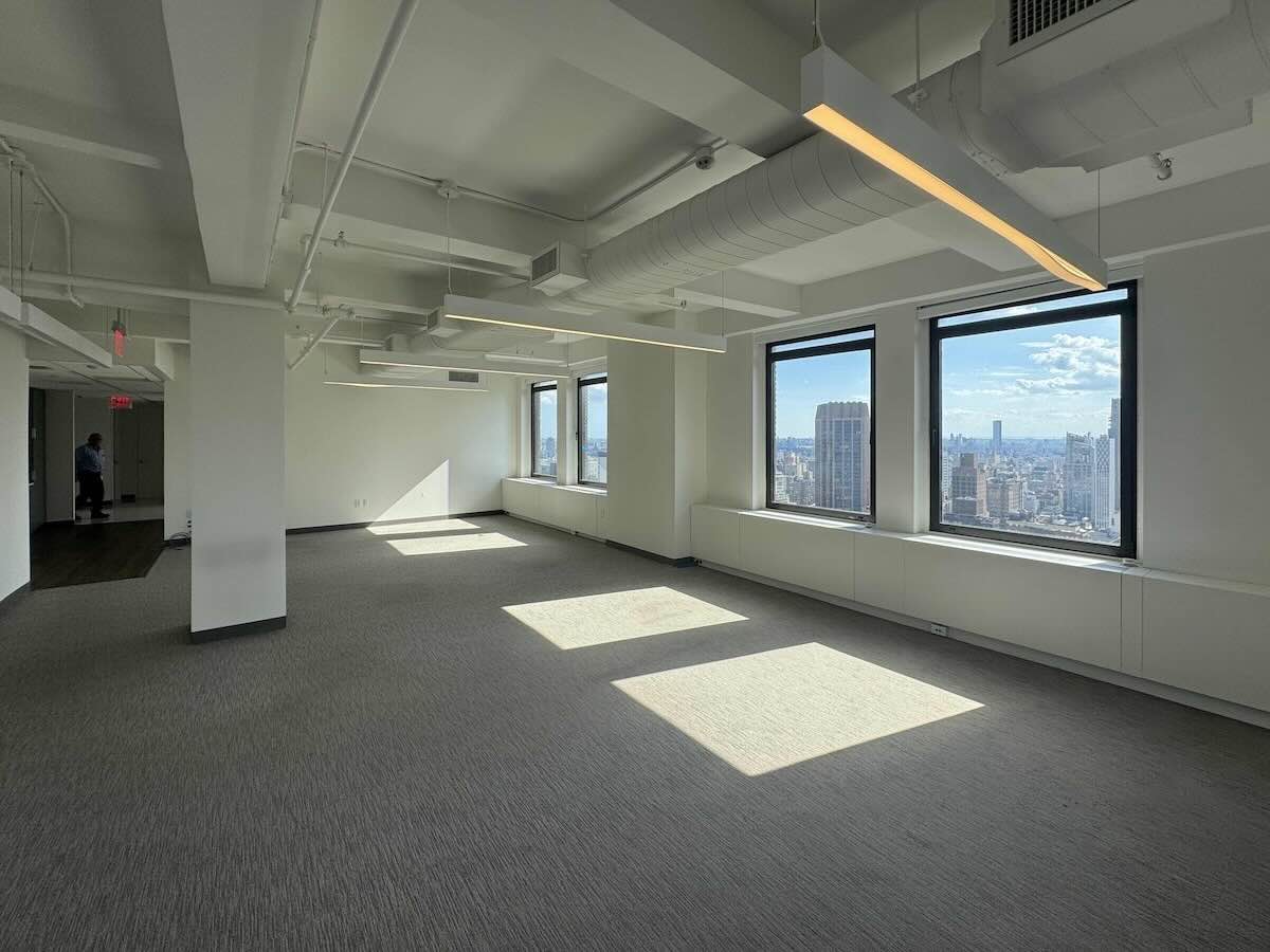 Modern empty office, large windows, gray carpet, white walls, skyline views.