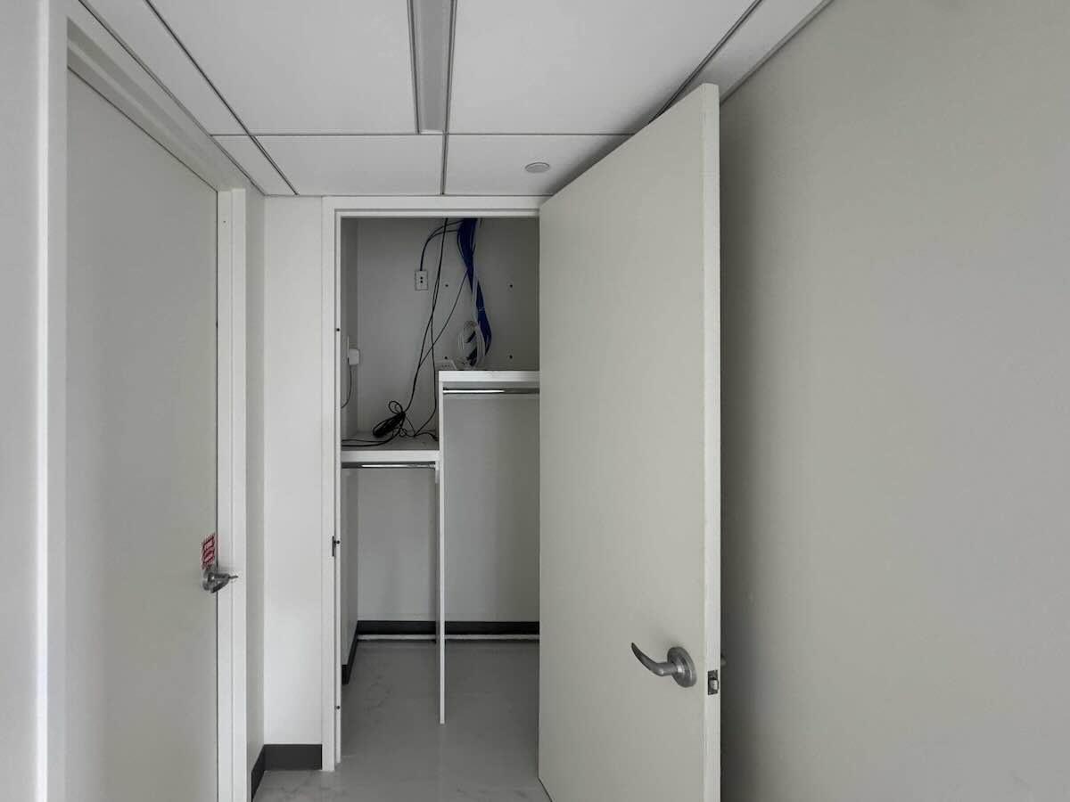 Beige door ajar on 33rd floor shows closet with cables, shelves; empty office, white walls, closed doors each side.