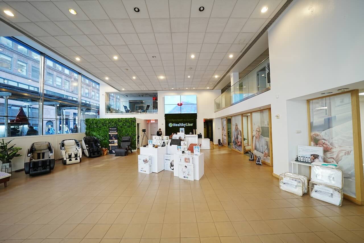 Modern showroom with massage chairs, product displays, and wellness ads. Natural light fills the space.