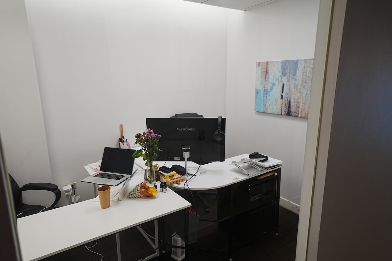 Tidy ground-level office with two desks, computers, art, and flowers.
