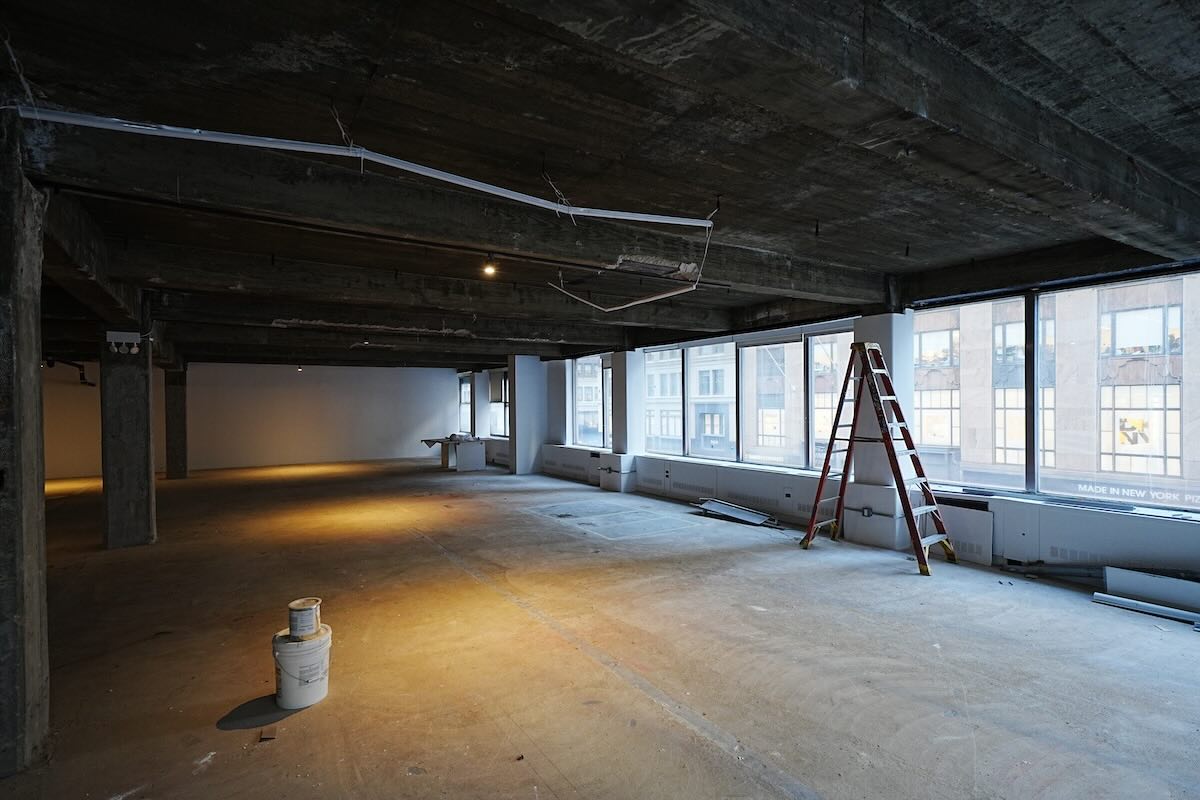 Empty unfinished room with concrete floor, large windows, ladder, exposed wires.