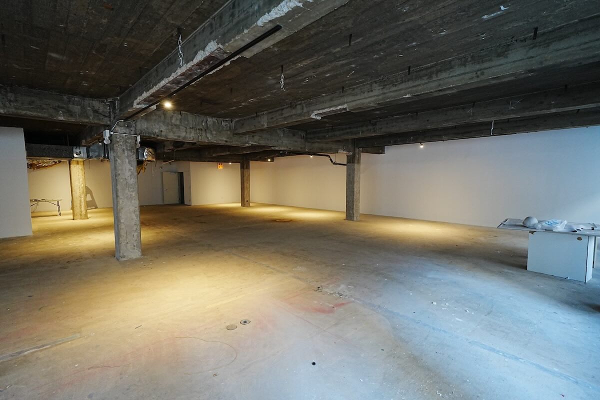 Empty industrial room, concrete floors, exposed beams, white walls, soft lighting. Some construction materials in corners at 515 Seventh Ave.