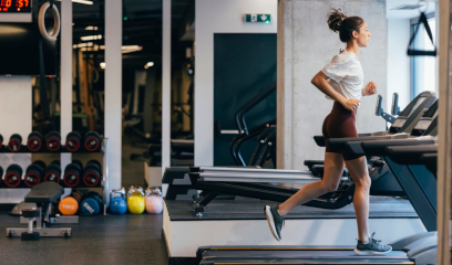 Woman in athletic wear runs on treadmill; organized gym gear in background.