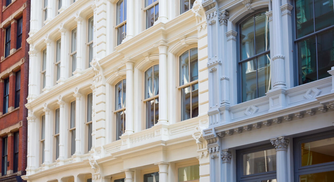 White cast-iron SoHo facade with large windows beside red brick building.