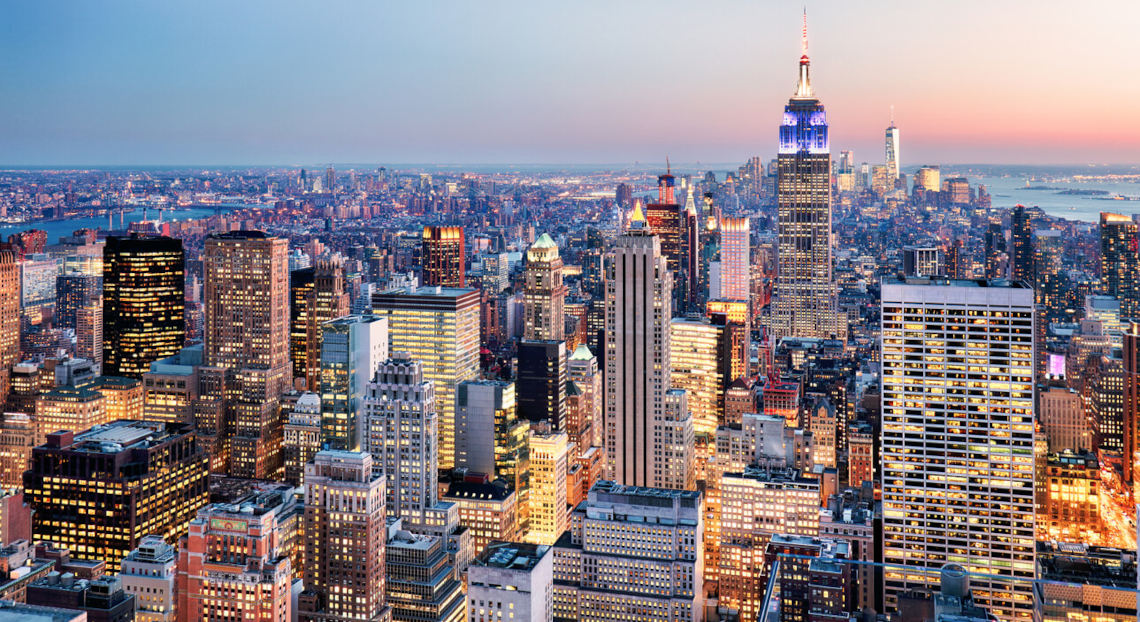 NYC skyline at dusk with glowing skyscrapers, including Empire State Building.