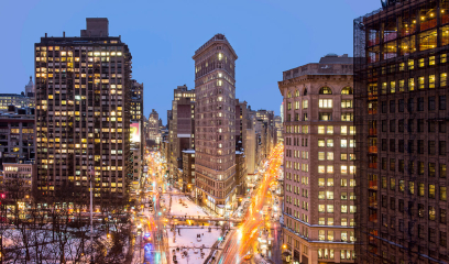 Flatiron Building at dusk, NYC, surrounded by lit streets and snowy ground.