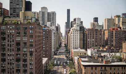 Midtown Manhattan, New York City street with tall modern offices, parked cars, trees, and clear sky.