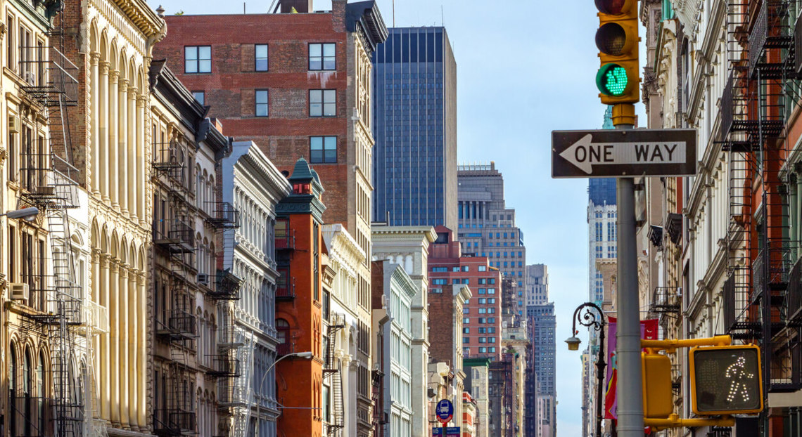 Manhattan city street with tall buildings, traffic lights, and signs.