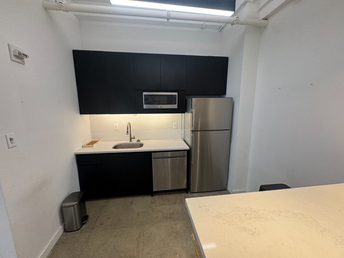 Modern kitchenette with black cabinets, stainless appliances, and white island.