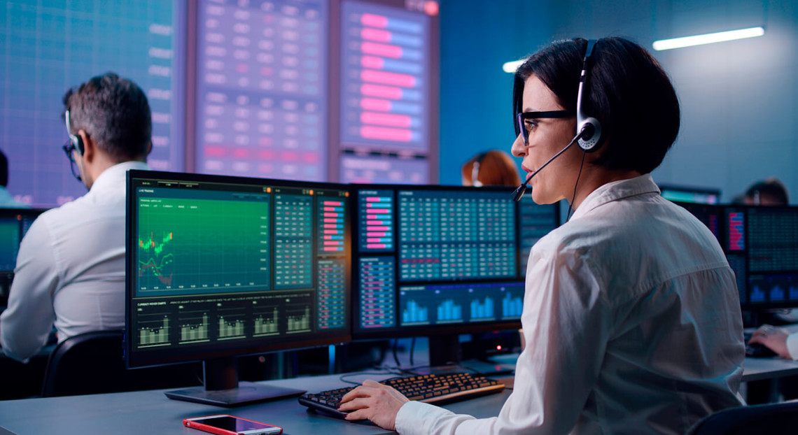 Woman in headset analyzes data charts at computer in modern control room.