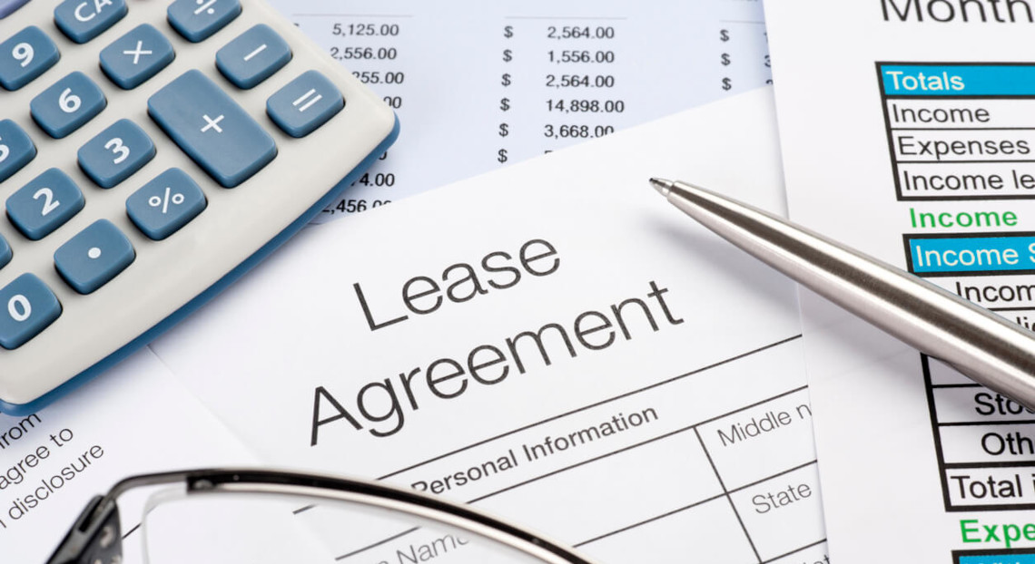 Lease agreement on desk with pen, calculator, papers, and glasses.