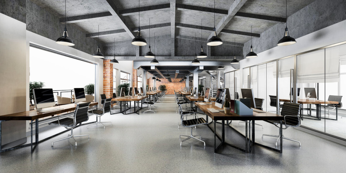 Modern office with rows of desks, large windows, black chairs, and exposed beams.