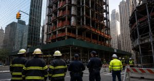 Firefighters, workers face a scaffolded building on a city street.