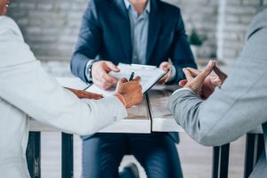 Three professionals at a table; one signs a document in NYC office.
