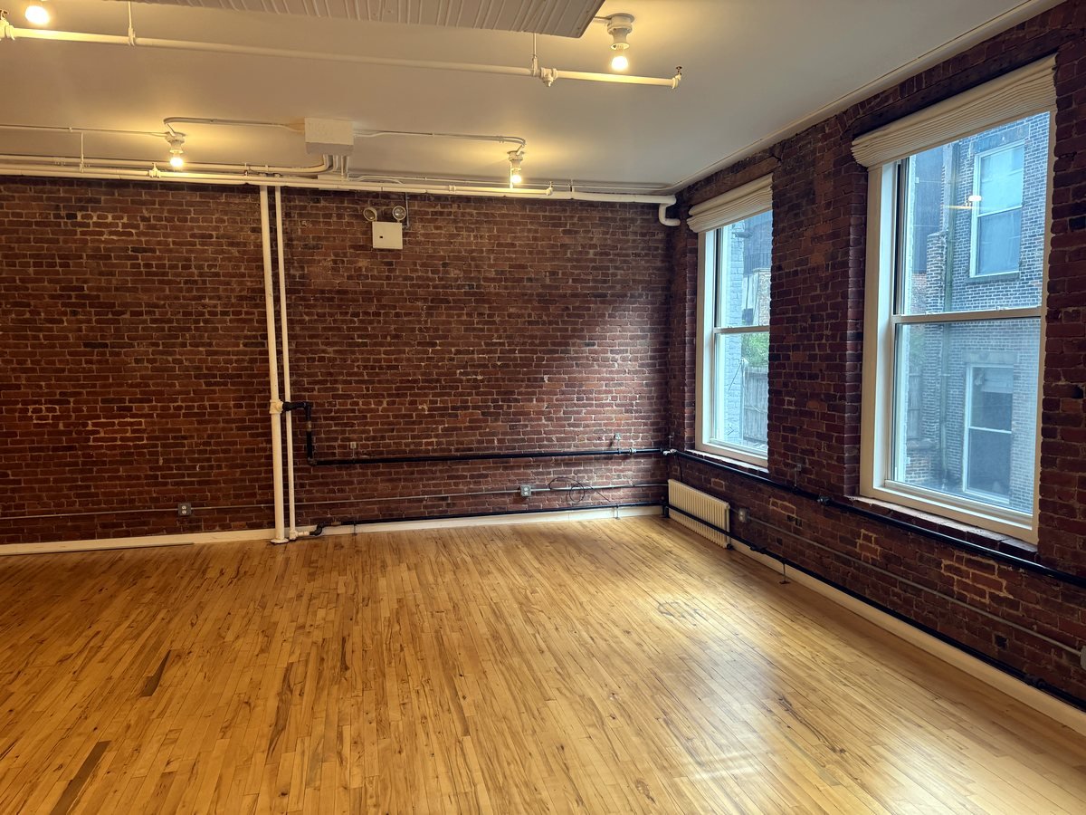 Bright open office with exposed brick and perimeter windows at 46 Greene Street